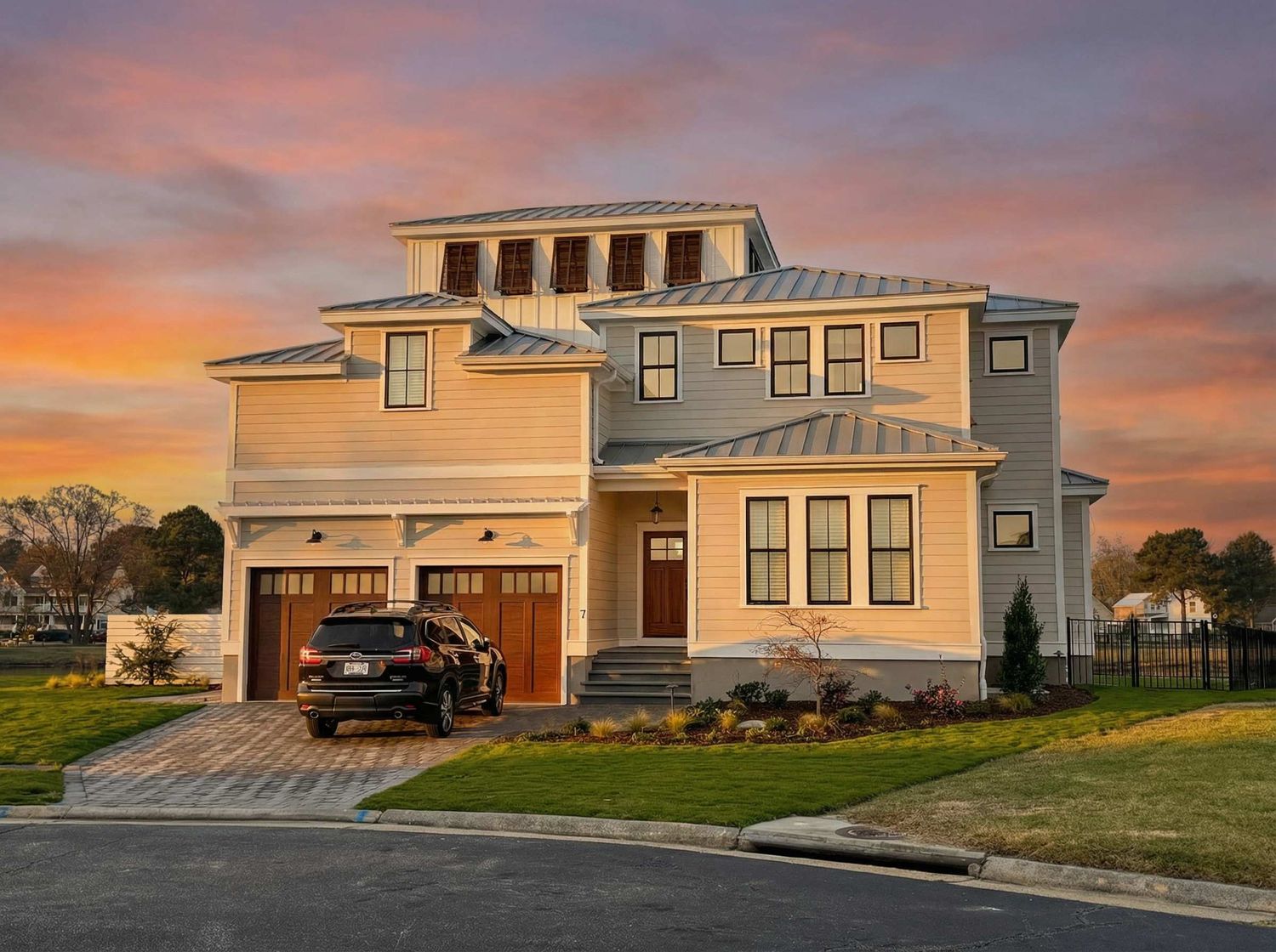 Exterior rendering of a coastal-style home with metal roof accents, double garage doors, and layered rooflines at sunset.