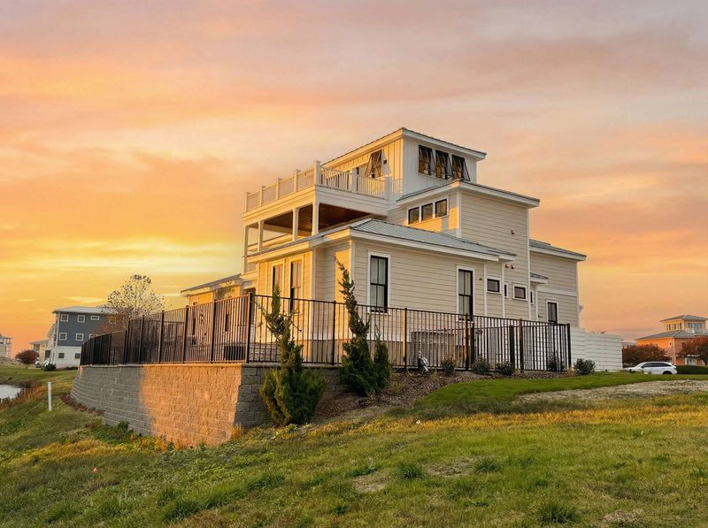 Exterior rendering of a coastal-style home with metal roof accents, double garage doors, and layered rooflines at sunset.