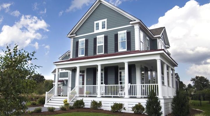 Front view of a three story white house with blue roof, wraparound porch, large windows and landscaped yard.