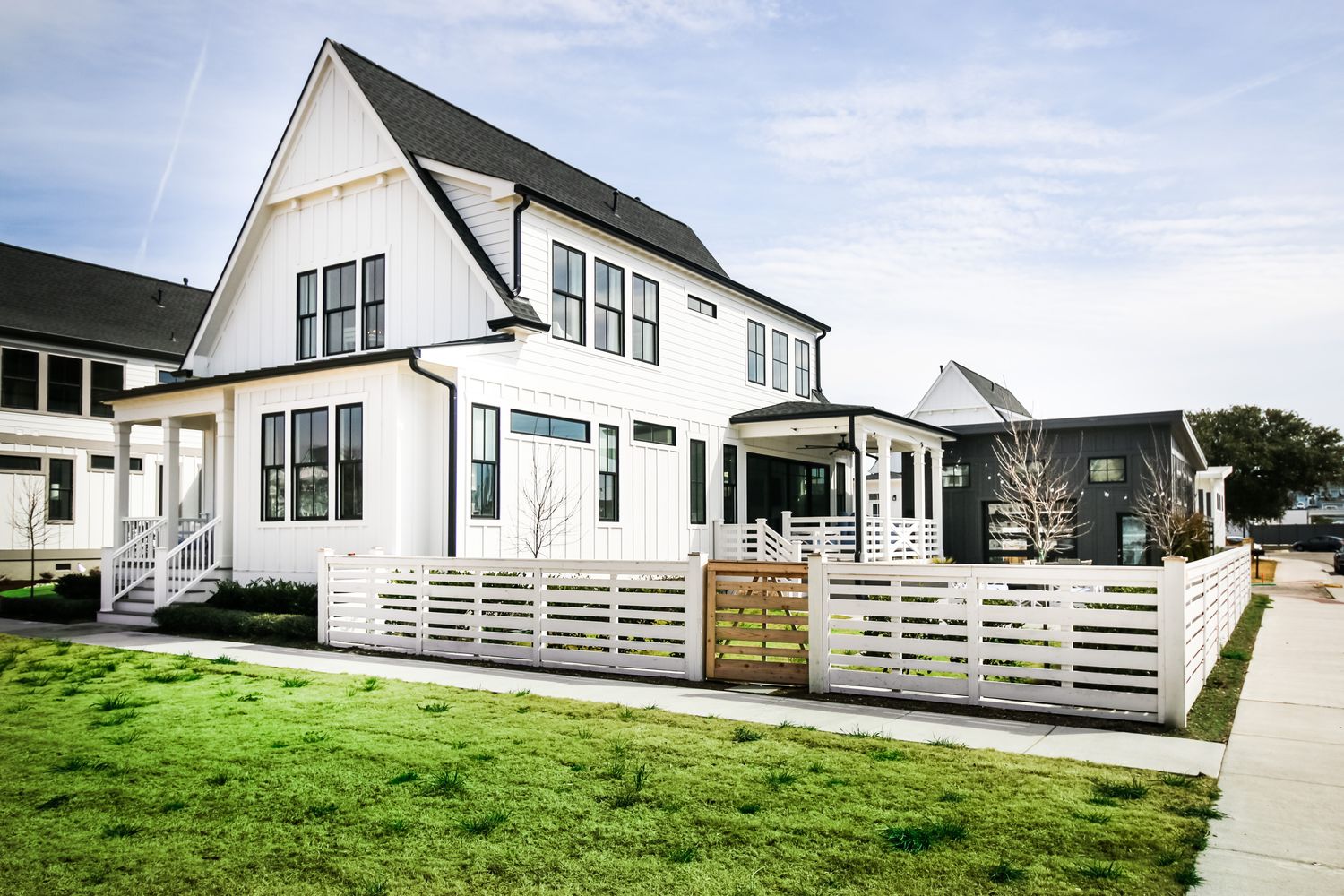 Exterior rendering of a farmhouse-style home plan with white board-and-batten siding, black window trim, and fenced yard.