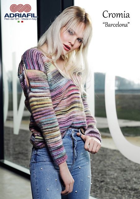 A woman is wearing a knitted sweater in a variegated pink, blue, yellow and grey yarn.