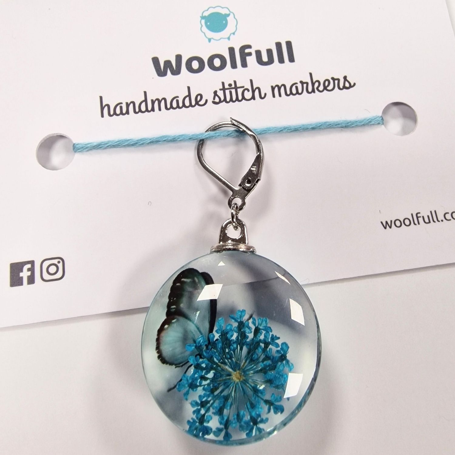 A round glass stitch marker with a blue butterfly and flower design in them.