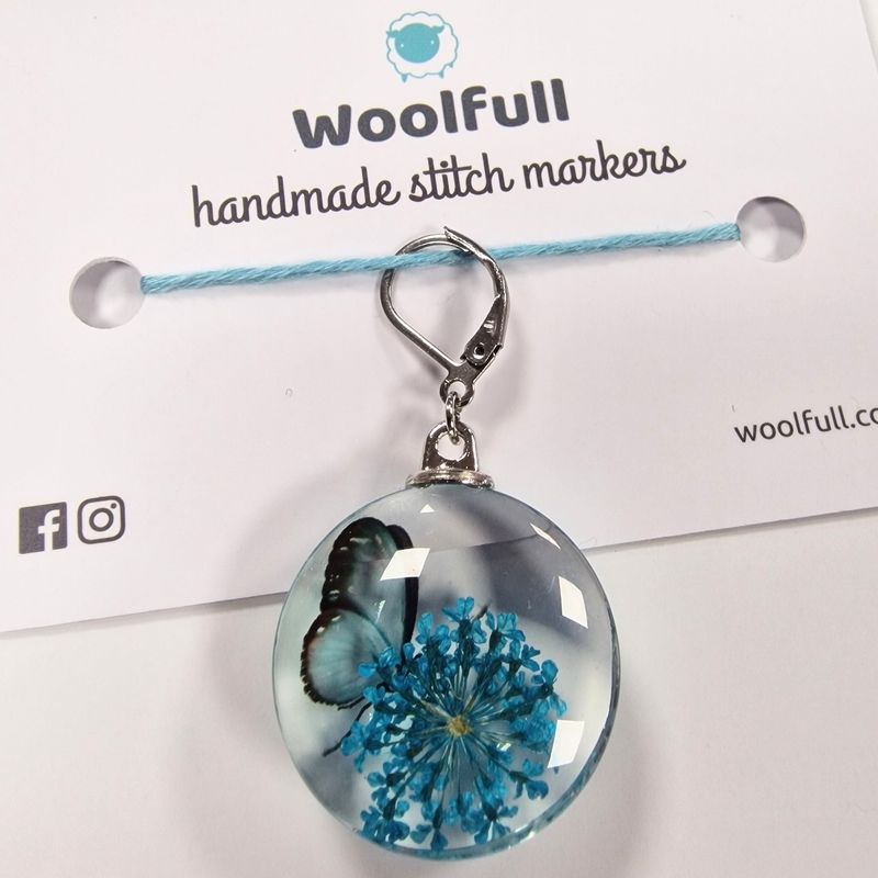 A round glass stitch marker with a blue butterfly and flower design in them.
