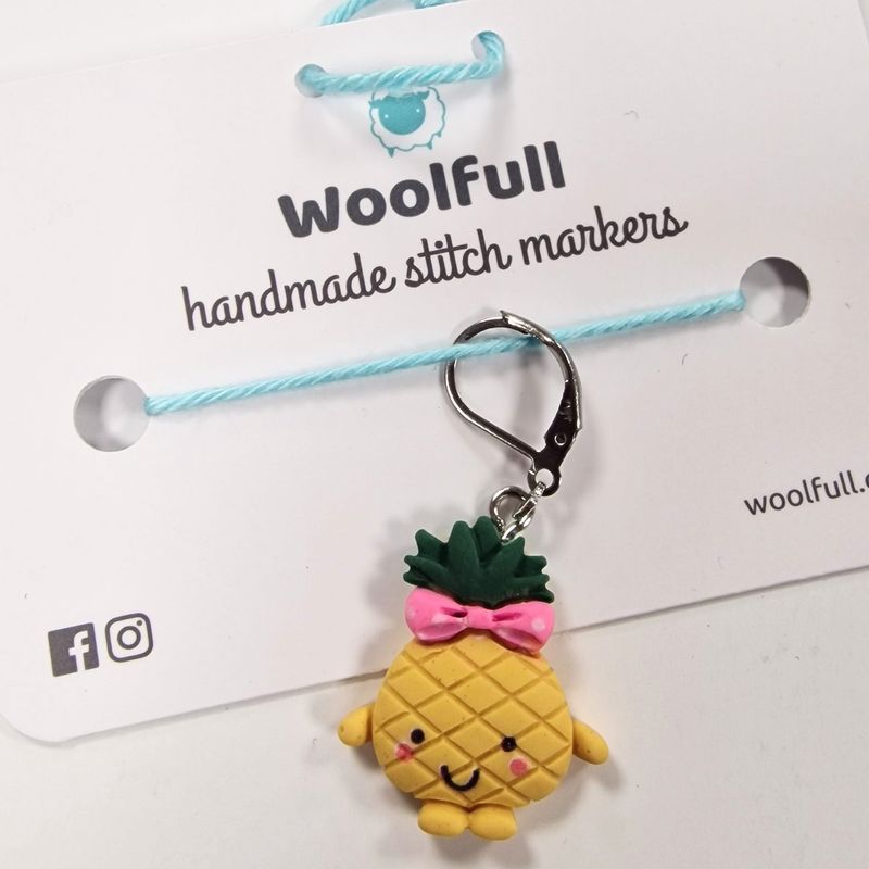 A pineapple shaped stitch marker with a smiley face and a bow.