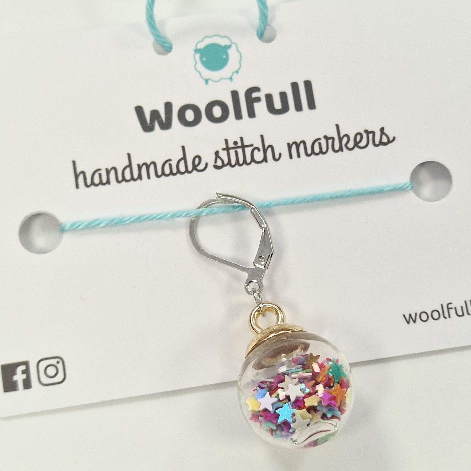 A glass ball stitch marker filled with rainbow star shaped confetti.