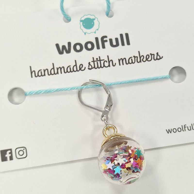 A glass ball stitch marker filled with rainbow star shaped confetti.