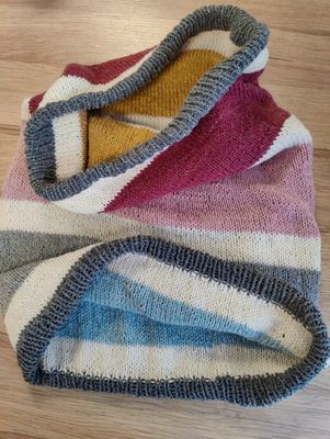 A knitted cowl in grey, cream, pink, blue and yellow stripes.