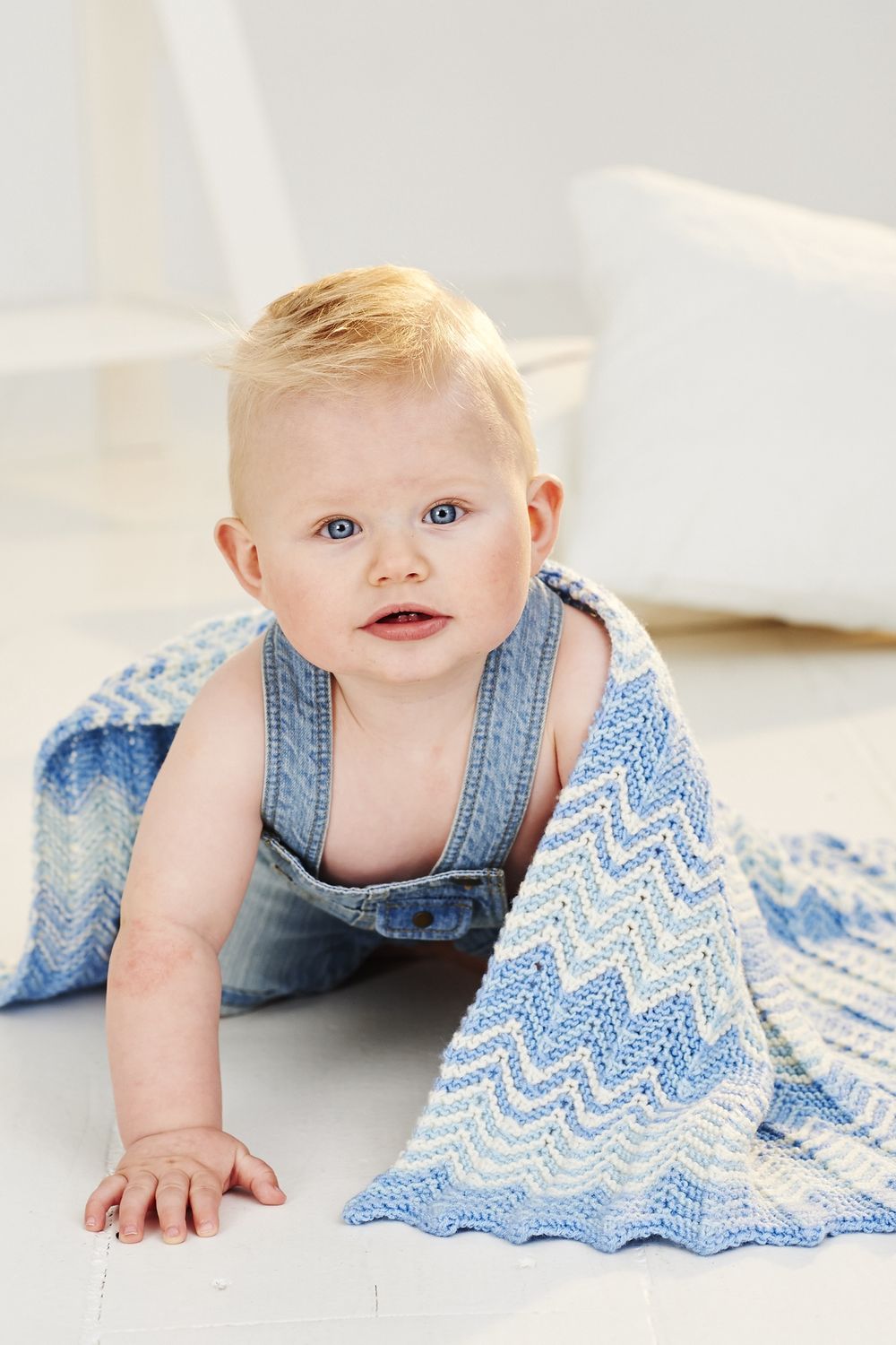 A baby is wearing a blue zig zag pattern knitted blanket.