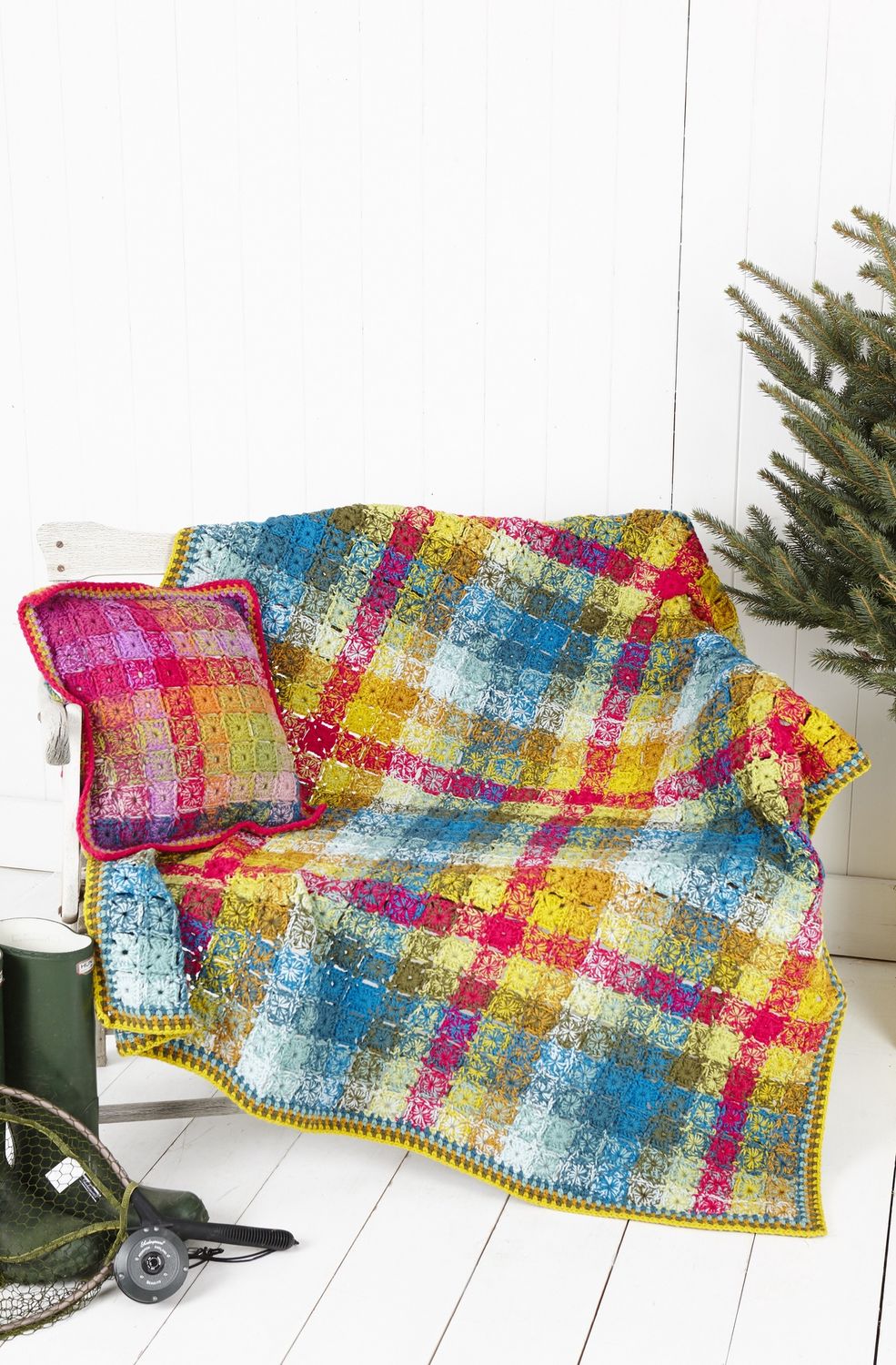 A crocheted blanket made up of small colourful squares, in a layout designed to mimic tartan.