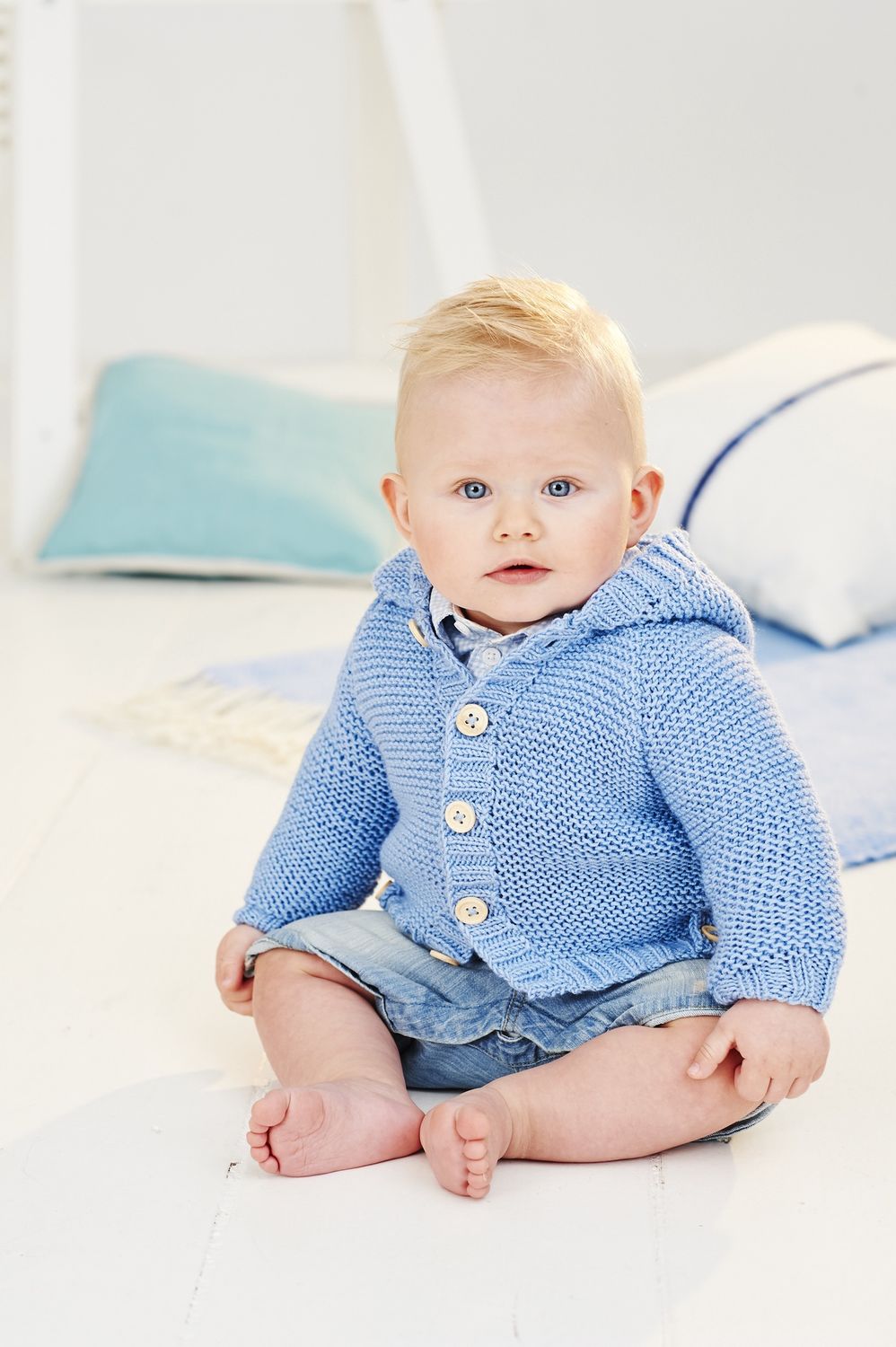 A baby is wearing a blue knitted cardigan.