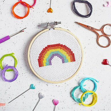 A small cross stitch with a rainbow design surrounded by threads, scissors and other accessories.