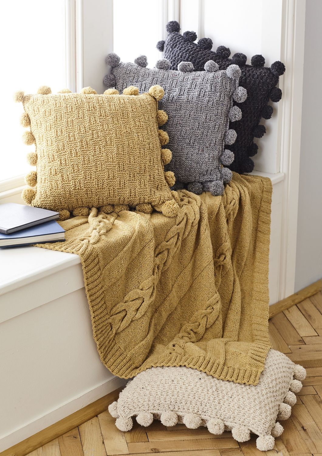 A mustard yellow cable knit blanket and mustard yellow, cream and grey knitted cushions.