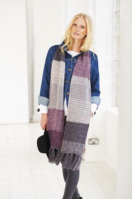 A woman is wearing a knitted scarf in a variegated purple and grey yarn.