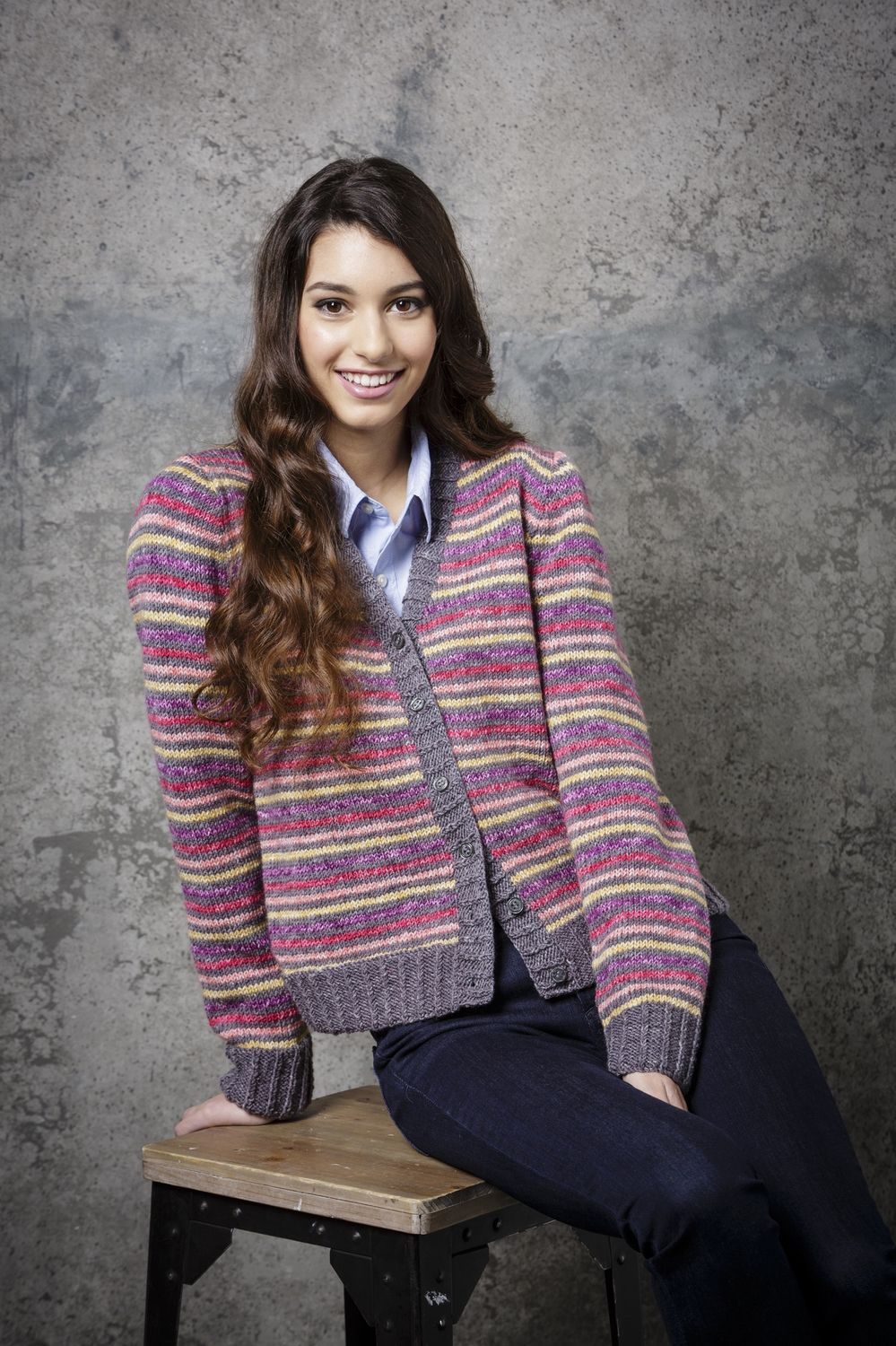 A woman is wearing a grey knitted cardigan with pink, purple and yellow stripes.