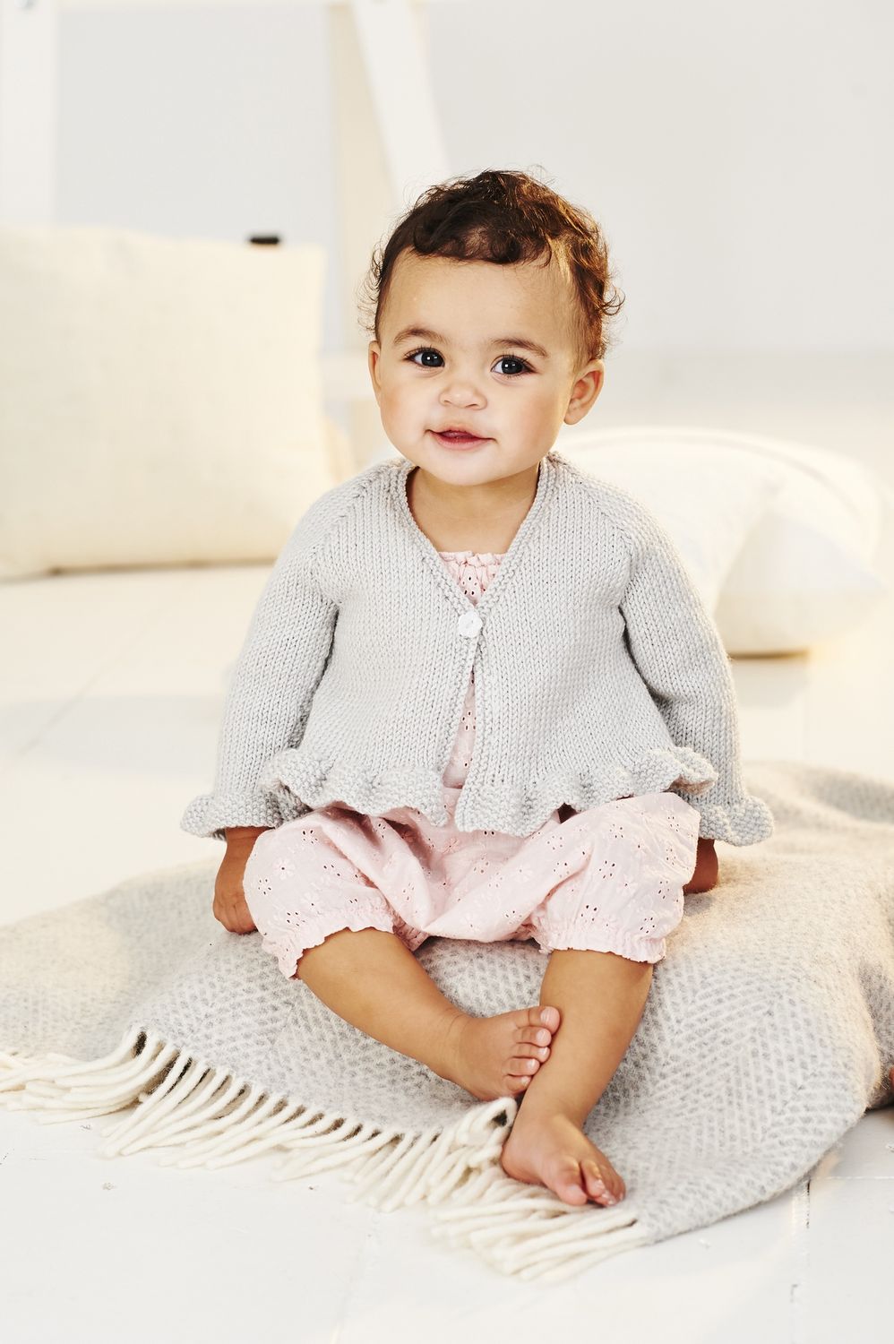A baby is wearing a light grey knitted cardigan.