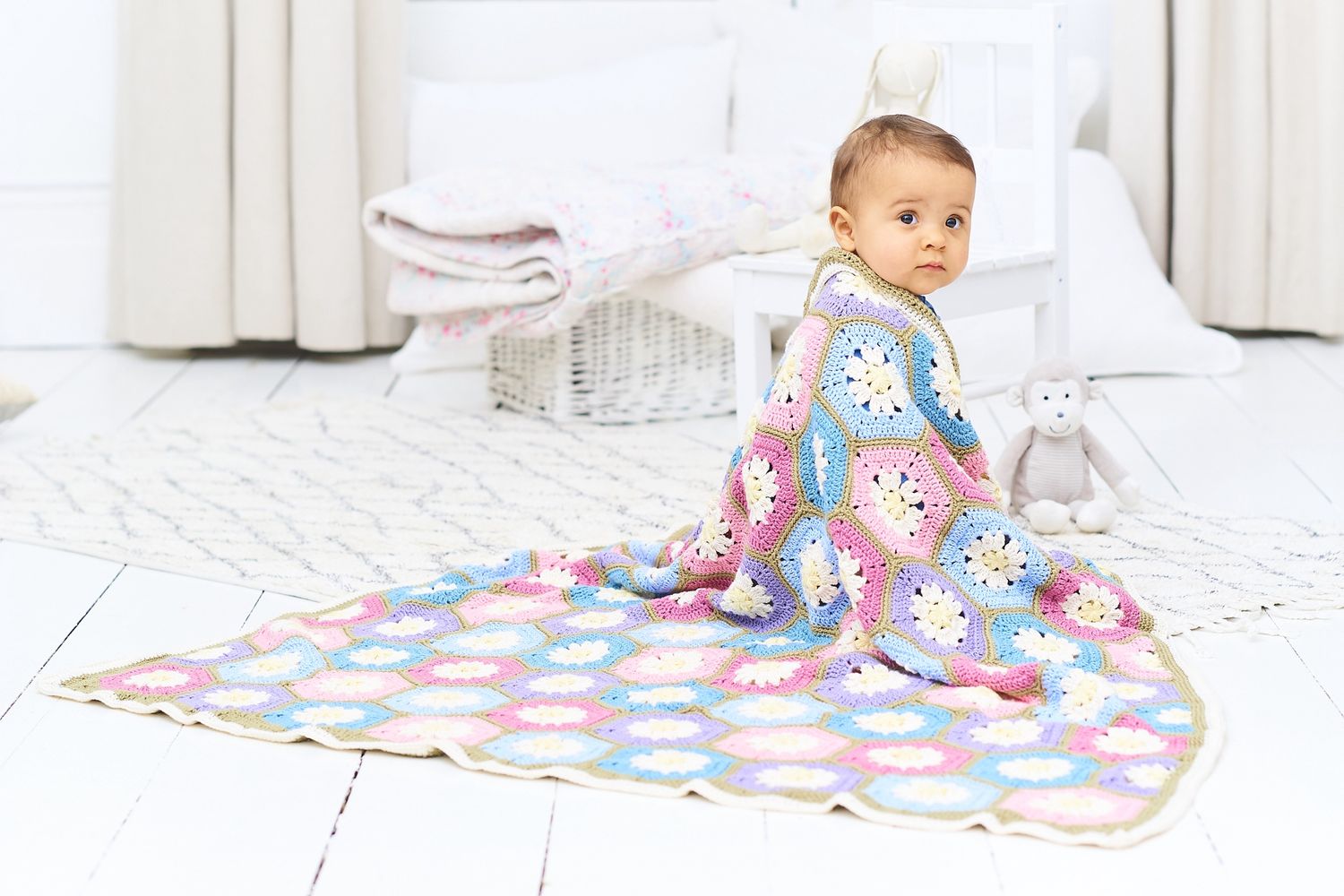 A baby is wrapped in a crocheted blanket made up oh pink, blue, purple and cream hexagons and joined together with green.