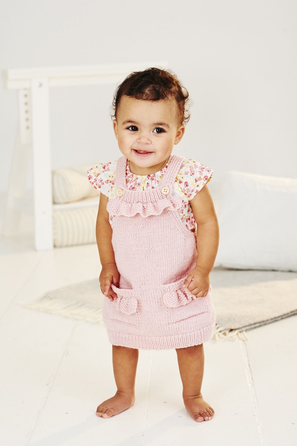 A baby is wearing a pale pink knitted dress.