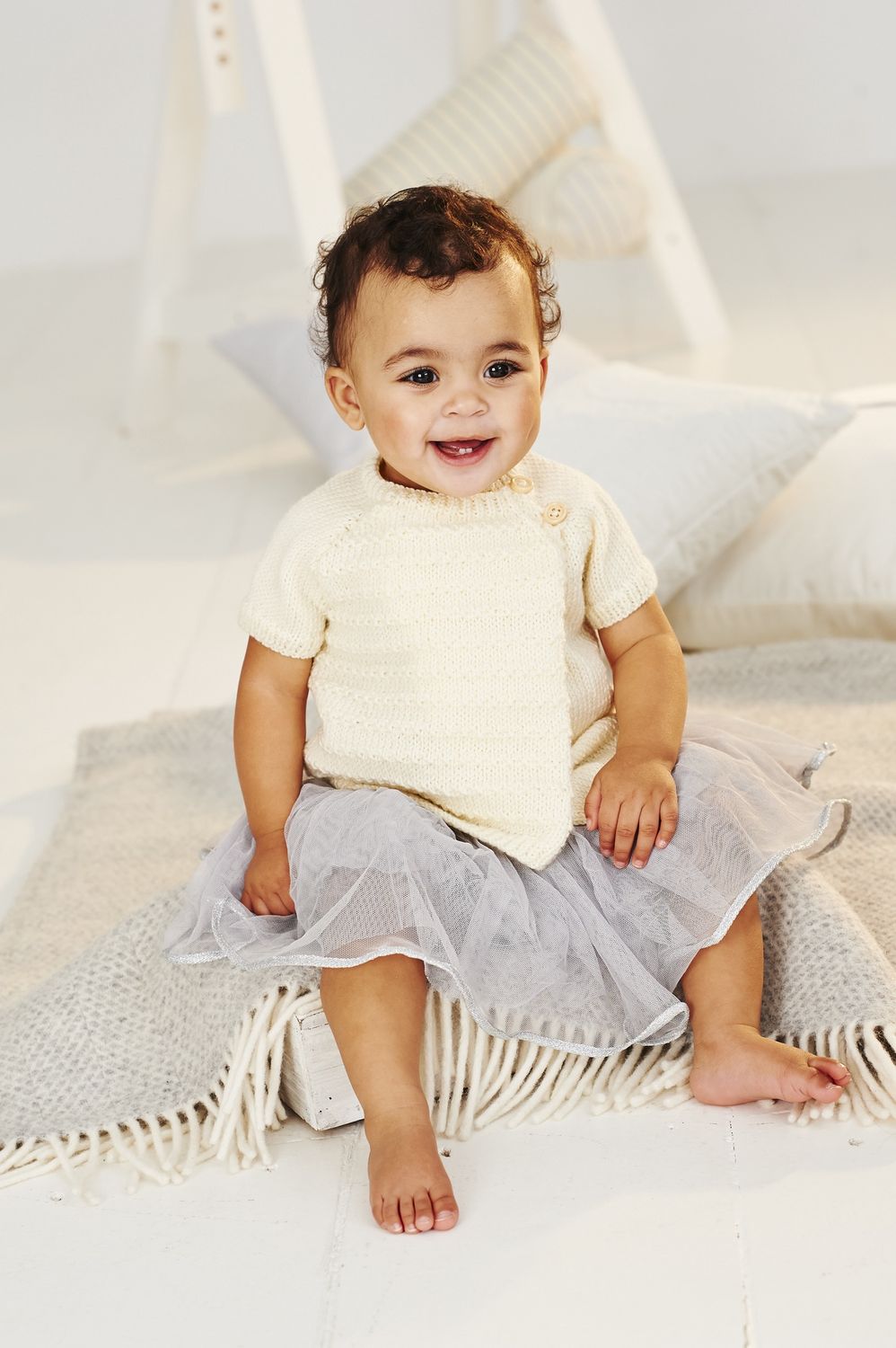 A baby is wearing a cream knitted cardigan.