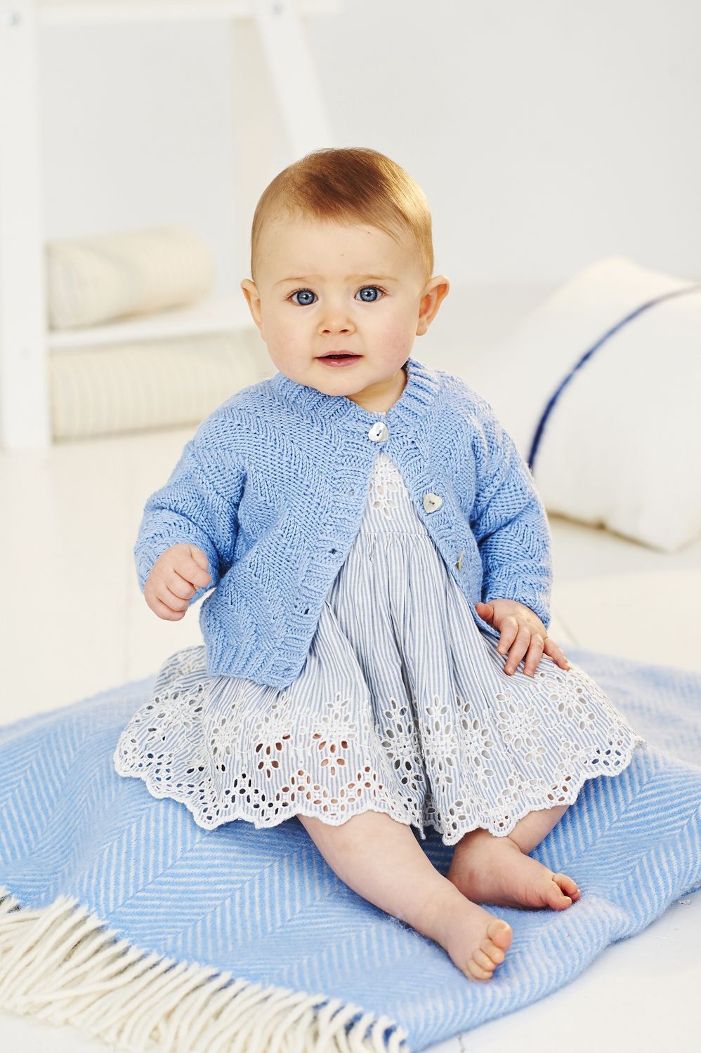 A baby is wearing a blue knitted cardigan.