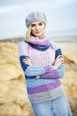 A woman is wearing a knitted sweater and matching cowl in a variegated pink, purple and blue yarn.