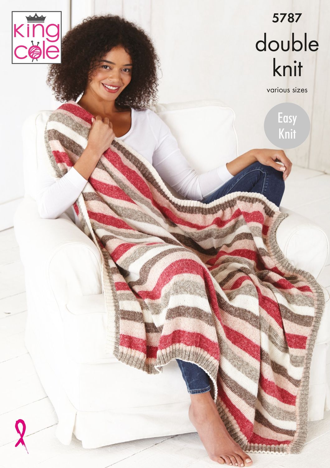 A woman is sat under a knitted blanket in red, cream and beige stripes.