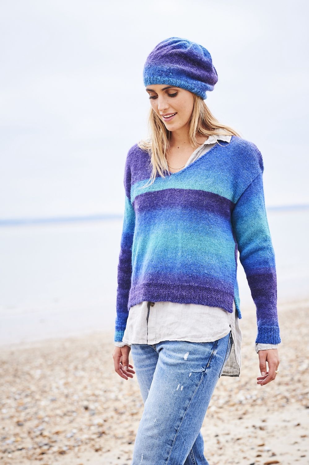 A woman is wearing a knitted sweater in a variegated blue and purple yarn.