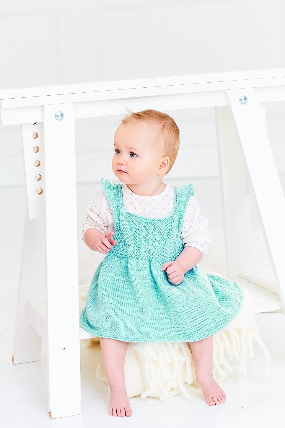 The front view of a baby wearing a blue knitted dress.