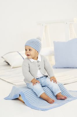 A baby is sitting on a blue knitted blanket while wearing a grey knitted cardigan and a blue knitted hat.