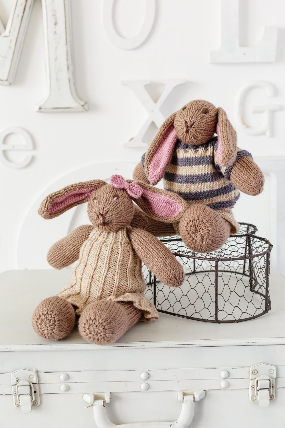 2 brown knitted rabbits wearing knitted clothes.