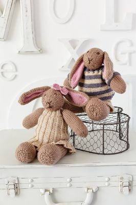 2 brown knitted rabbits wearing knitted clothes.