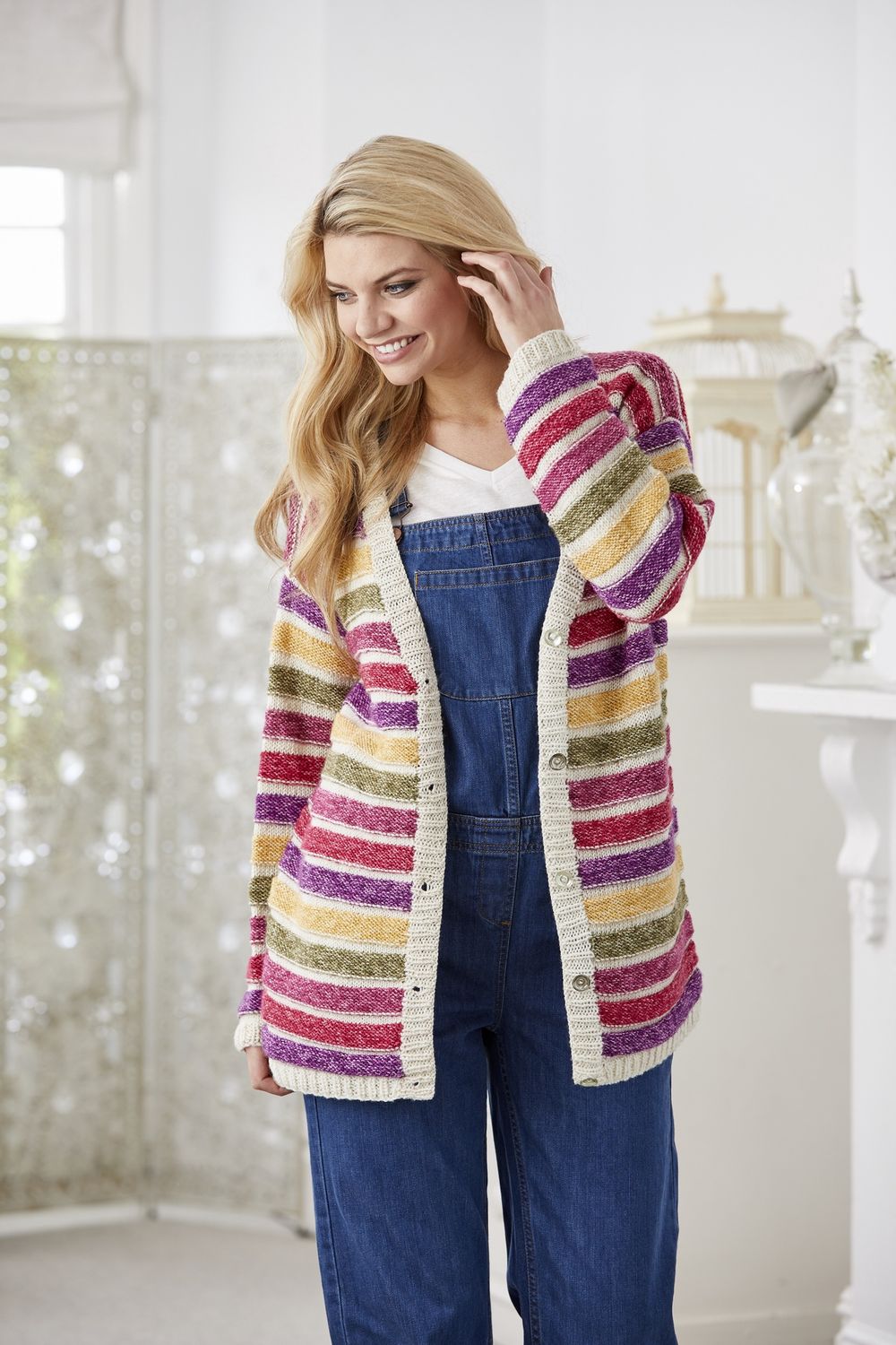 A woman is wearing a cream knitted cardigan with yellow, green, pink and purple stripes.