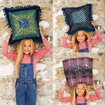 A girl is holding 3 crocheted cushions in variegated yarns.
