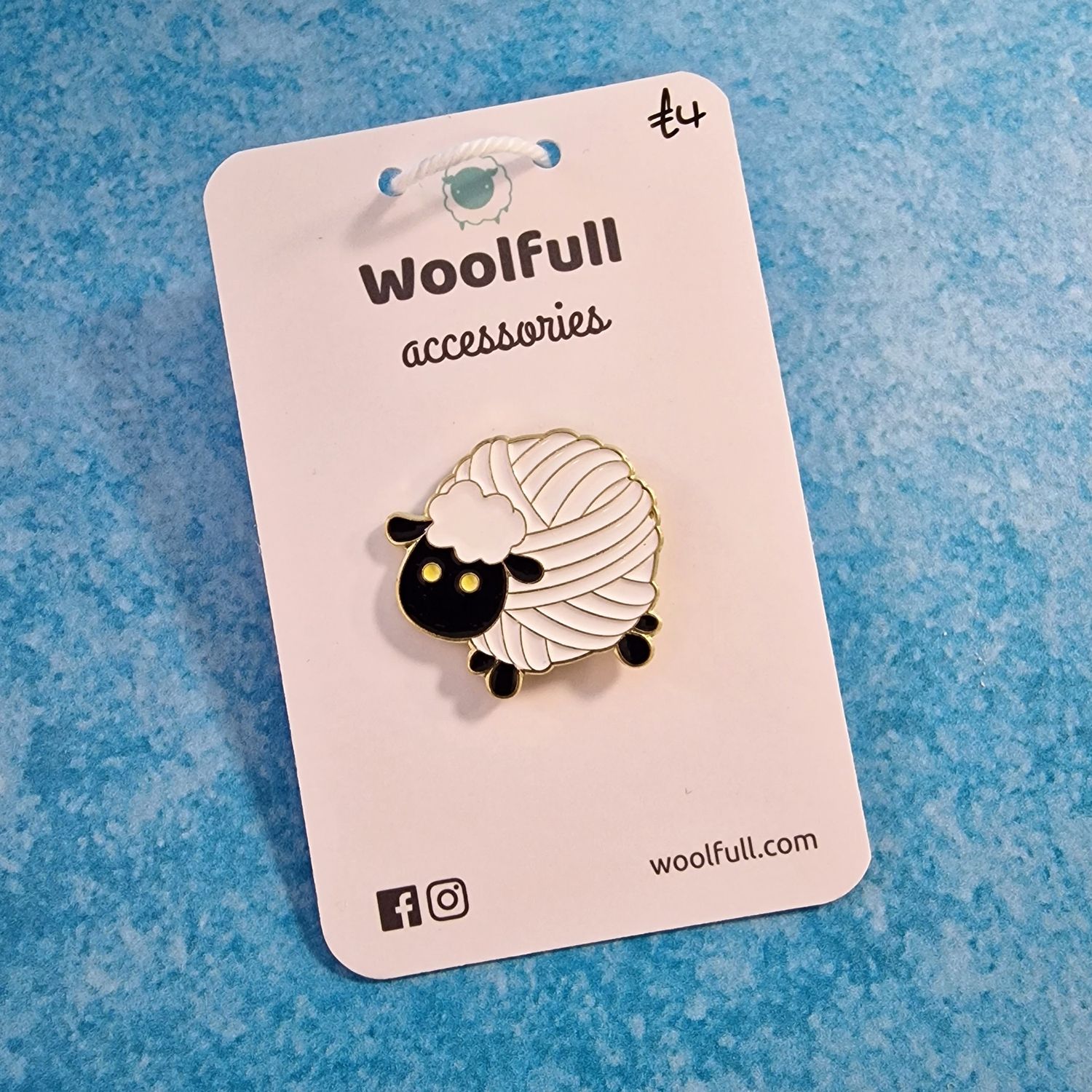 A blue background with a pin badge of a white sheep with a ball of yarn shaped body.