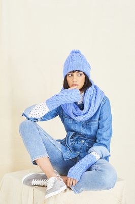 A woman is wearing a blue knitted hat, cowl and wristwarmers.