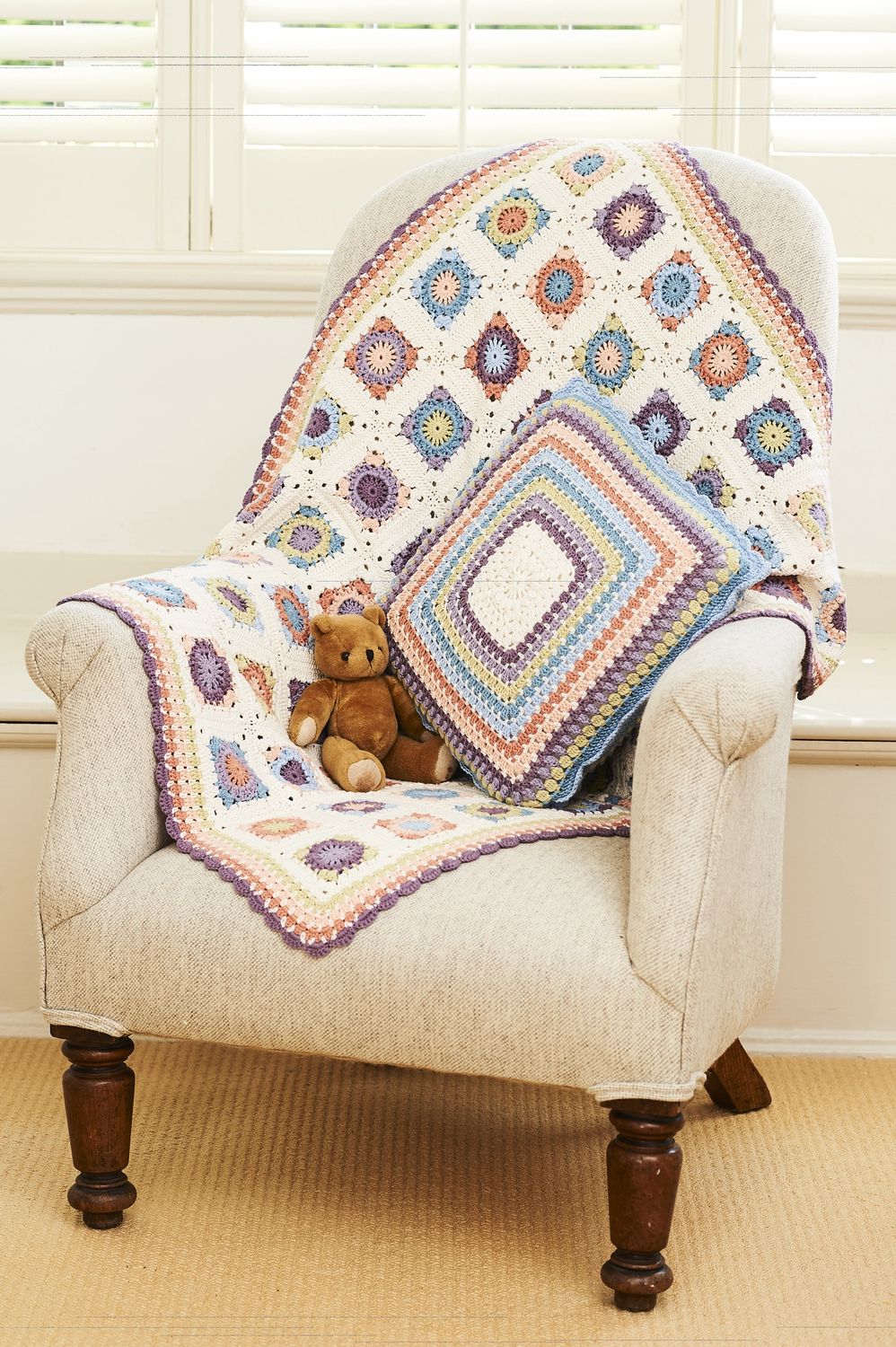 A crocheted blanket made up of cream, peach, blue, blue and green squares, alongside a matching cushion.