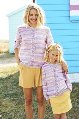 A woman and a girl are wearing matching knitted sweaters in a variegated pink, purple and cream yarn.