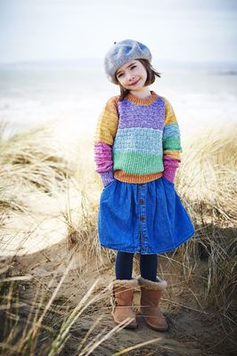 A girl is wearing a knitted sweater in a variegated blue, green, yellow, purple, pink and orange yarn.