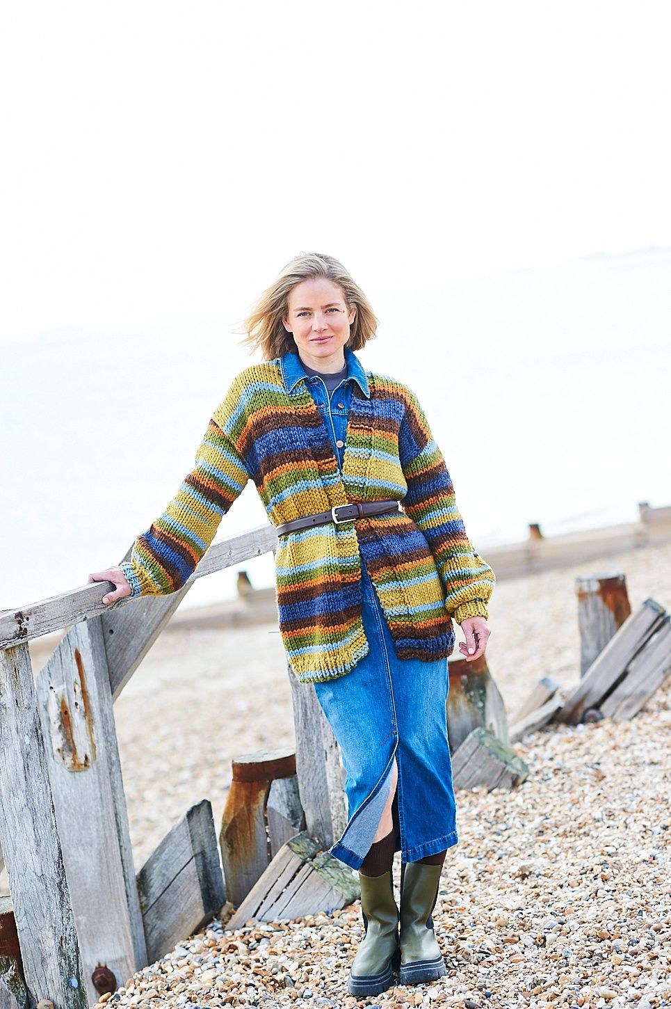 A woman is wearing a variegated long knitted cardigan in shades of blue, green, brown and orange.