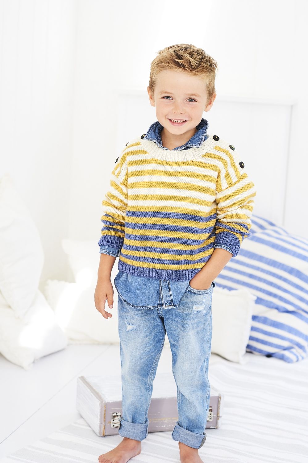 A boy is wearing a cream, yellow and blue stripy knitted sweater.