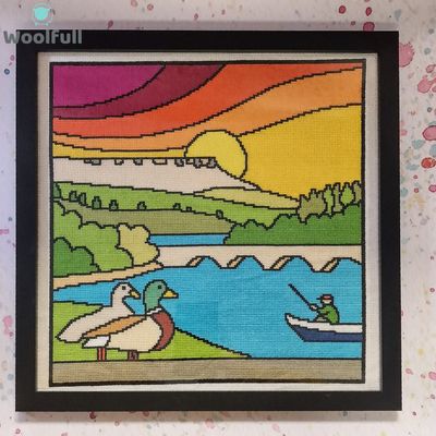 A framed cross stitch with a cartoon style design of Ladybower reservoir in the Peak District.