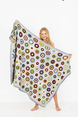 A woman is holding a crocheted blanket in grey, cream, yellow, green, purple, blue and red.