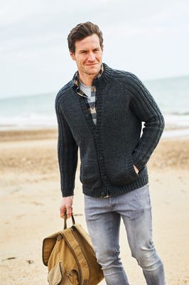 A man is wearing a black knitted cardigan with cable down the sleeves.