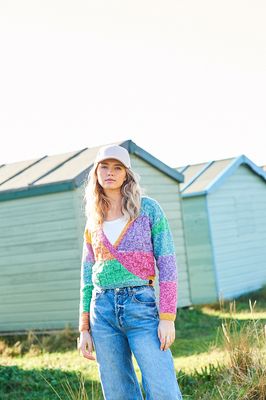 A woman is wearing a knitted wrap cardigan in shades of green, purple, yellow, pink and blue.