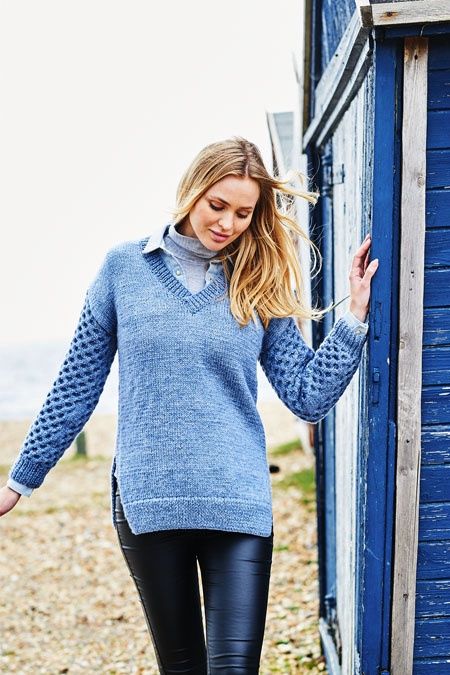 A woman on the beach is wearing a light blue sweater with a honeycomb pattern on the sleeves.