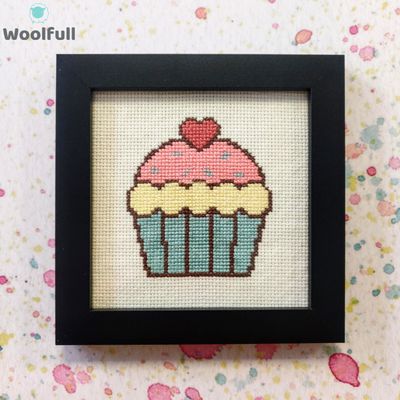 A framed cross stitch with a design of a cartoon style cupcake.