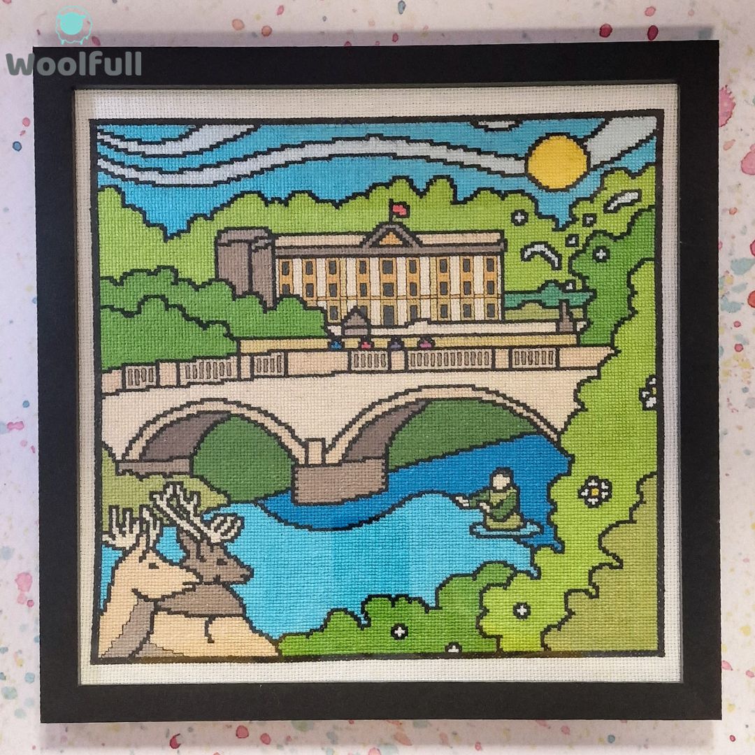 A framed cross stitch with a cartoon style design of Chatsworth House in the Peak District.
