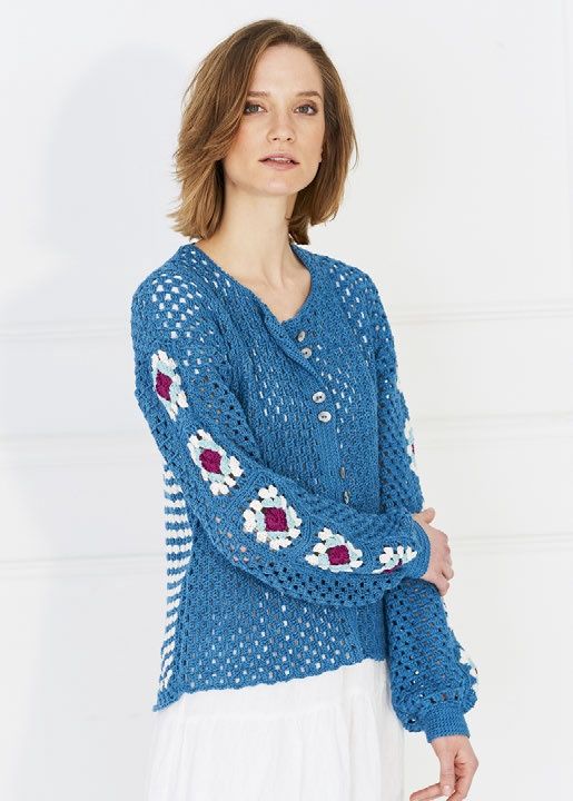 A woman is wearing a blue crocheted cardigan with granny squares on the back and sleeves.