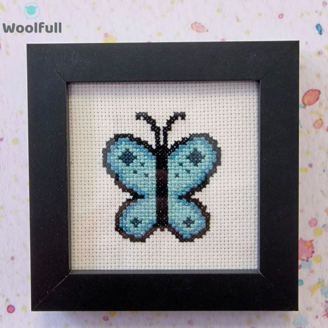 A framed cross stitch with a design of a blue cartoon style butterfly.