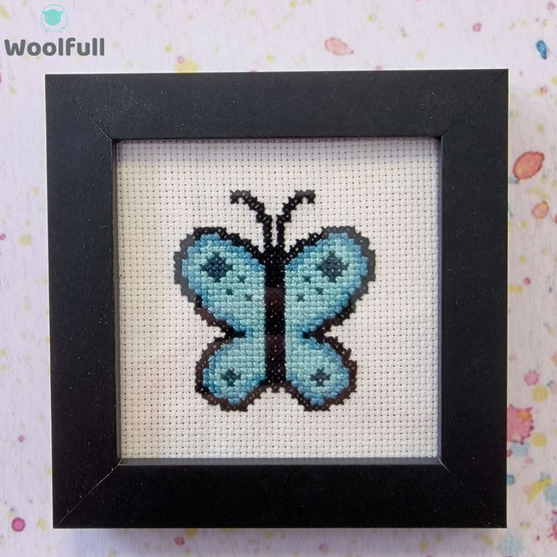 A framed cross stitch with a design of a blue cartoon style butterfly.