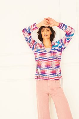 A woman is wearing a crocheted sweater in shades of pink, purple and blue.